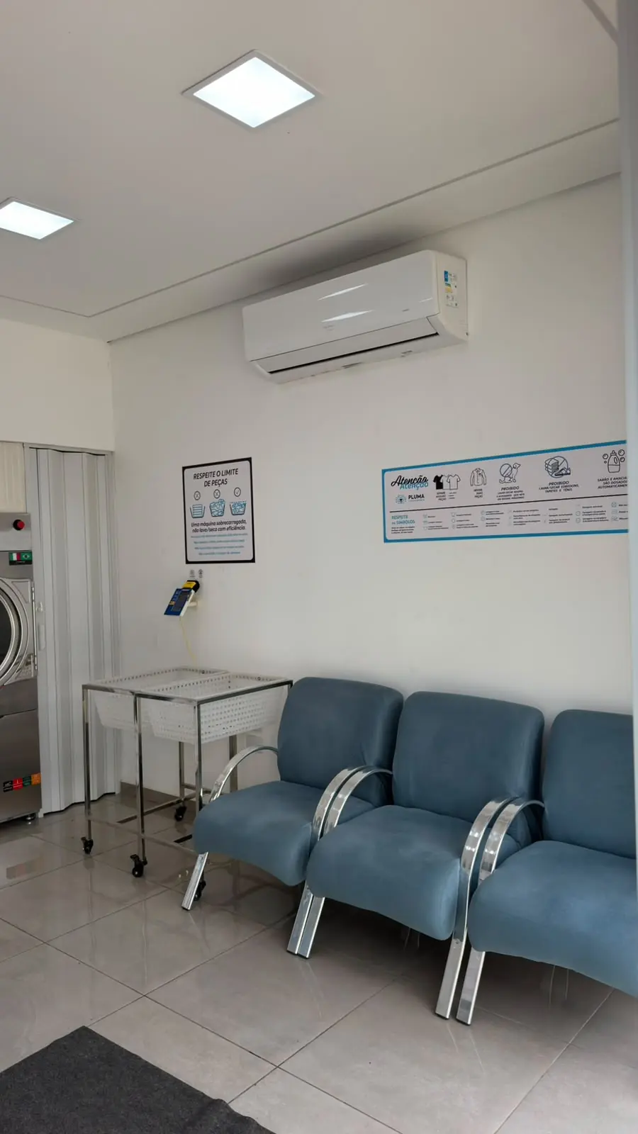 Sala de espera da Pluma Itaporanga com três poltronas azuis, ar-condicionado ligado e o painel de orientação na parede.
