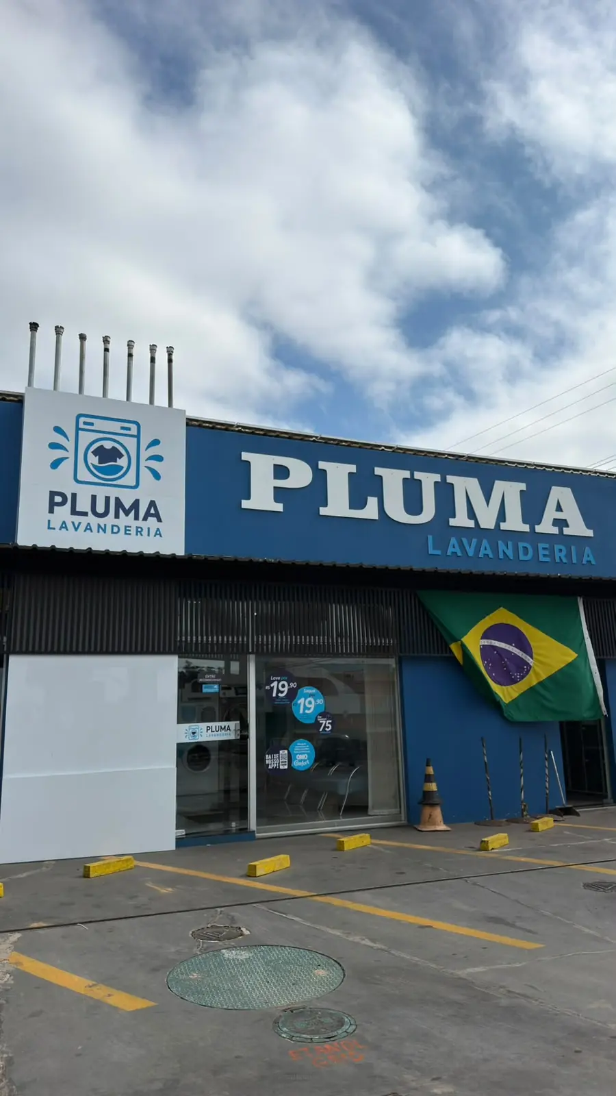 Fachada da Pluma Lavanderia em Itaporanga: letreiro branco PLUMA sobre o prédio azul do Auto Posto Pluma, com estacionamento na frente.