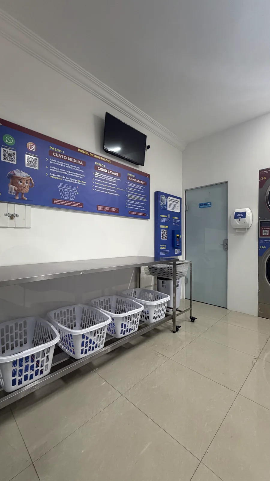 Painel de instruções da Pluma Itararé na parede, com os passos de cesto medida, como lavar e como secar, ao lado da mesa de inox com cestos.